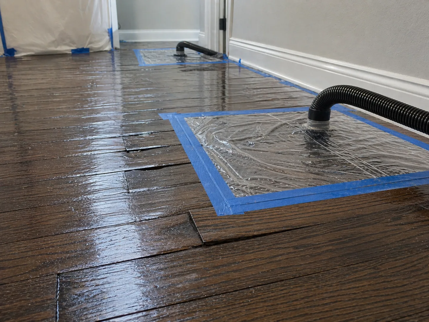 Water-damaged hardwood flooring with drying mats taped down for restoration